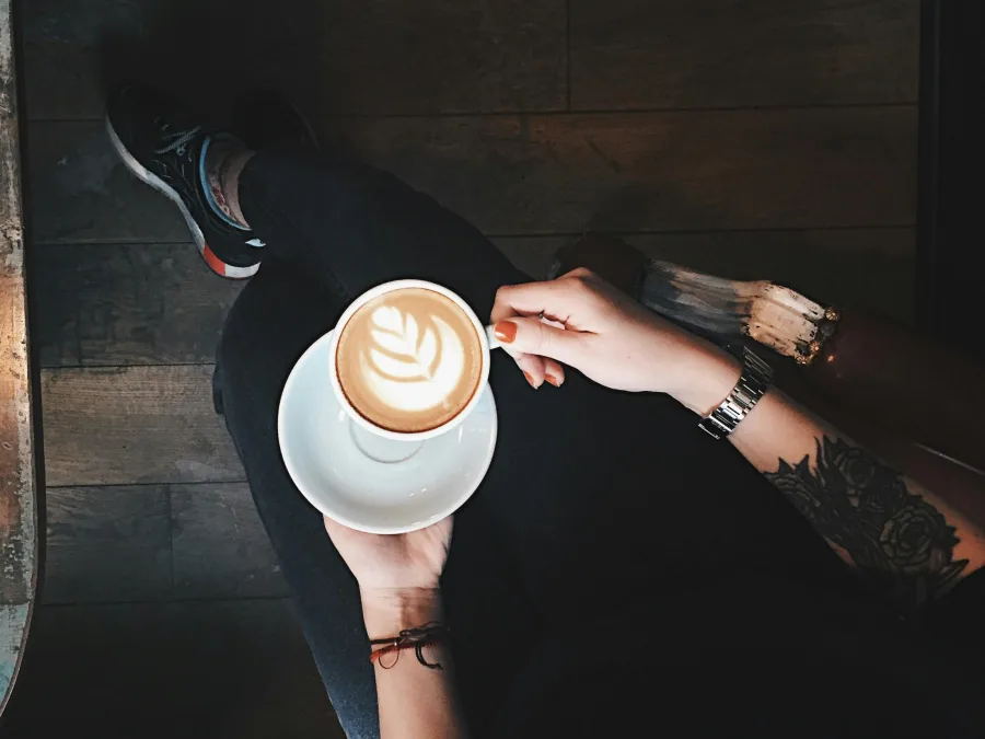 Κάτοψη ατόμου που κρατάει ένα φλιτζάνι καφέ latte με σχέδιο στην επιφάνεια.