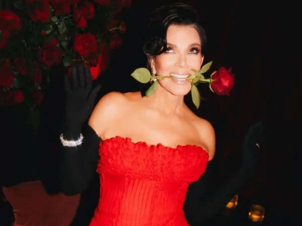 Η Kris Jenner με κόκκινο φόρεμα και ένα τριαντάφυλλο στο στόμα.