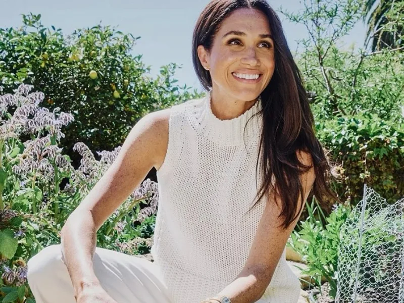Η Meghan Markle χαμογελάει σε εξωτερικό χώρο, με το άρθρο να αναφέρεται στη συνεργασία της με το Netflix.