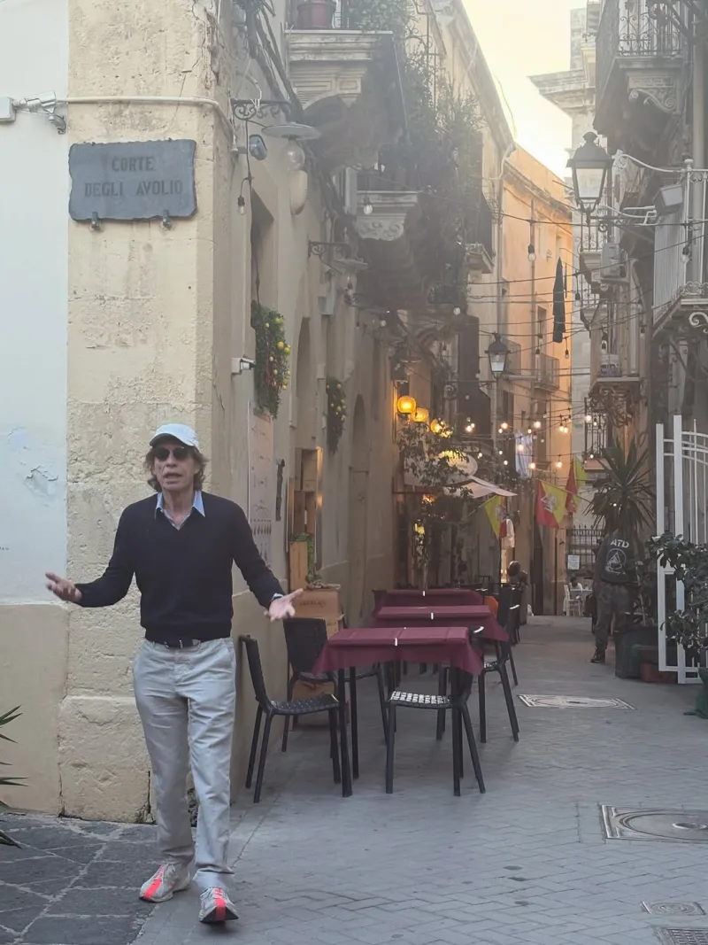 Ο Mick Jagger σε γραφικό σοκάκι με τραπέζια εστιατορίου.