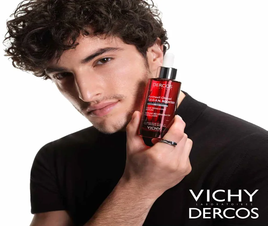 Άνδρας με σγουρά μαλλιά κρατάει τον ορό Vichy Dercos Aminexil Clinical R.E.G.E.N. Booster.