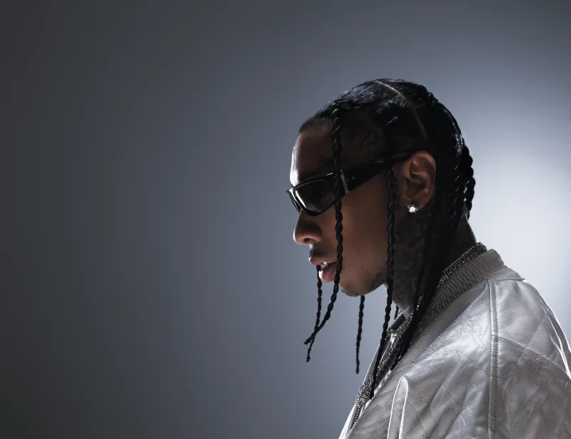 Προφίλ του Tyga με πλεξούδες, γυαλιά ηλίου και λευκό μπουφάν.