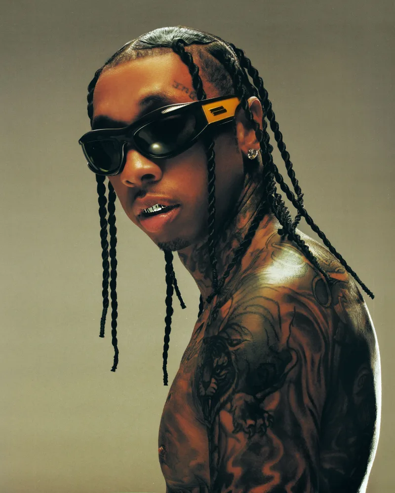 Ο Tyga με μαύρα γυαλιά ηλίου, πλεξούδες και τατουάζ.