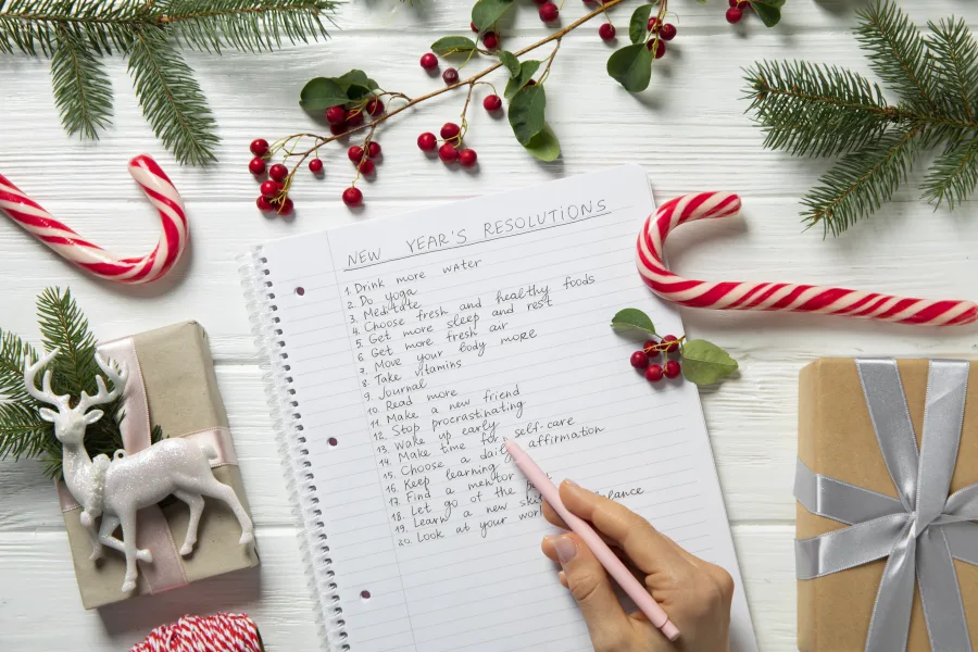Λίστα με New Year's Resolutions σε τετράδιο με χριστουγεννιάτικη διακόσμηση.