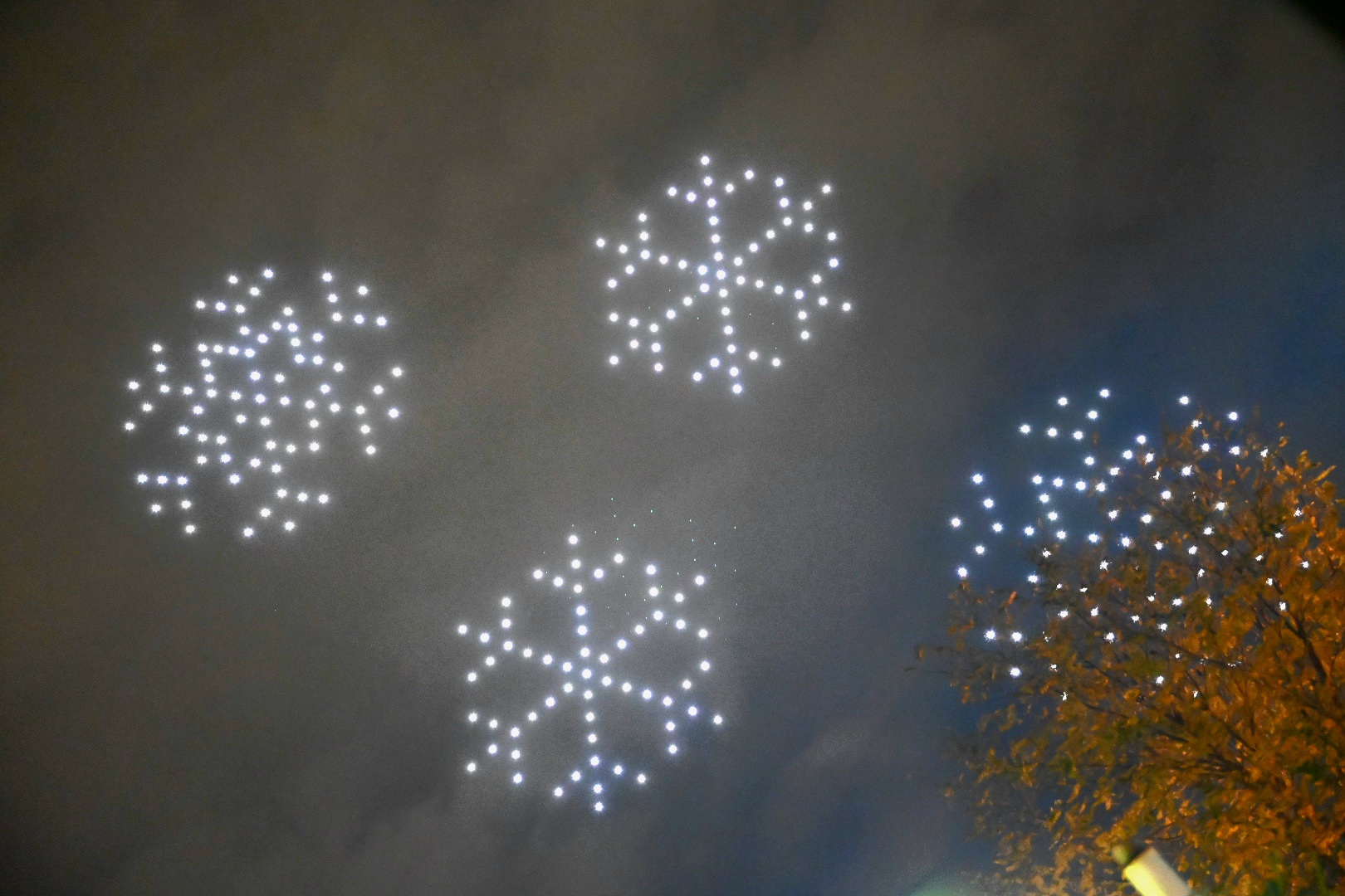 Drone show με φωτεινές νιφάδες χιονιού στον νυχτερινό ουρανό.