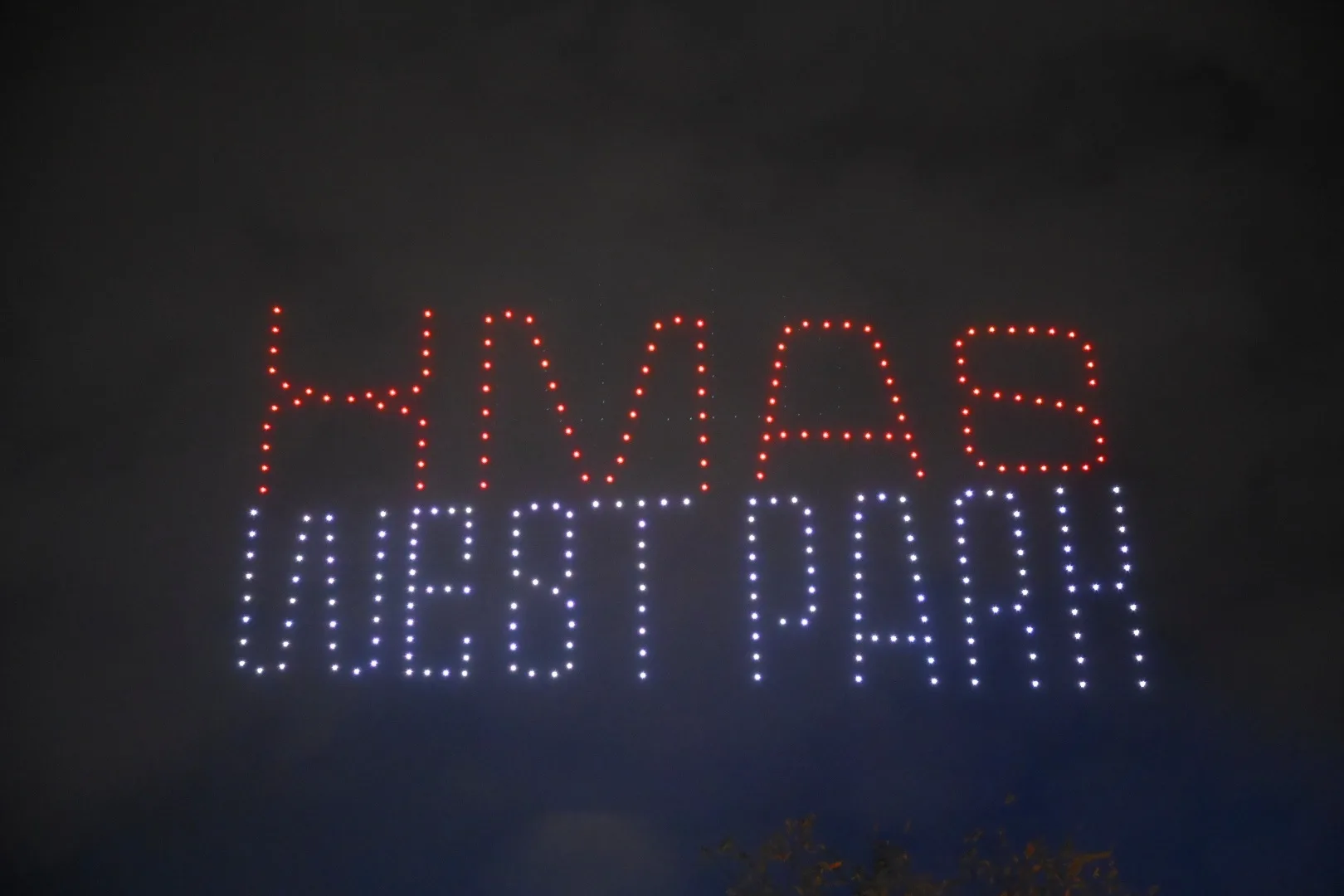 Drone show στον νυχτερινό ουρανό που σχηματίζει τις λέξεις XMAS WEST PARK με κόκκινα και λευκά φώτα.