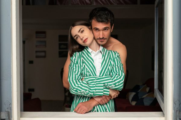 Η Emily Cooper με πράσινο ριγέ σακάκι στην αγκαλιά ενός άνδρα.