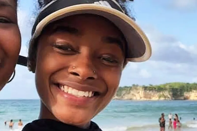 Η Imani Dia Smith χαμογελάει στην παραλία φορώντας καπέλο.