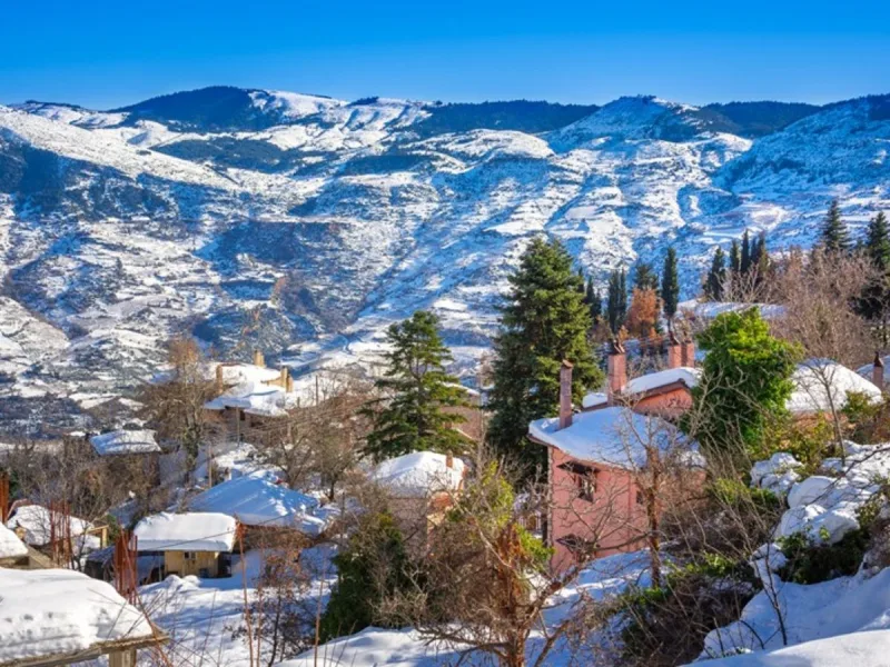 Χιονισμένο χωριό με σπίτια και δέντρα, ιδανικό για μονοήμερες εκδρομές κοντά στην Αθήνα.