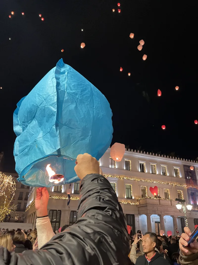Άνθρωποι κρατούν ένα γαλάζιο φαναράκι στην πλατεία Κοτζιά τη Νύχτα των Ευχών.