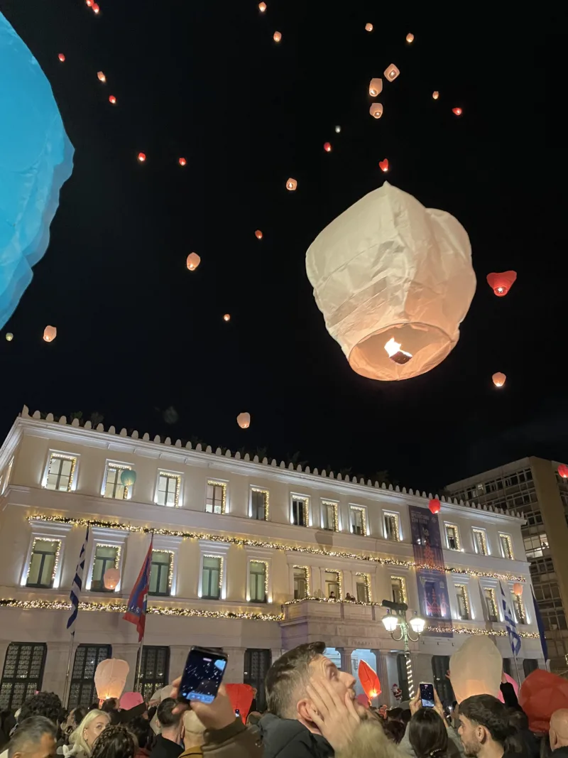 Πλήθος κόσμου στην πλατεία Κοτζιά απελευθερώνει φαναράκια στον νυχτερινό ουρανό.