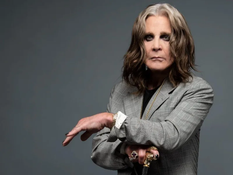 Ο Ozzy Osbourne σε στούντιο πορτρέτο με γκρι καρό σακάκι και μπαστούνι.