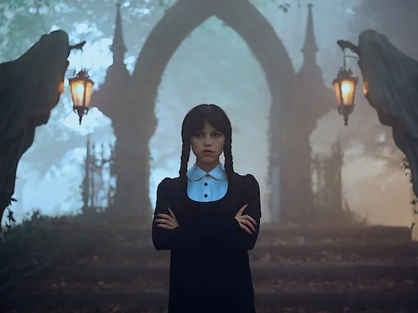 Η Jenna Ortega ως Wednesday Addams μπροστά από μια πέτρινη αψίδα σε ομιχλώδες τοπίο.