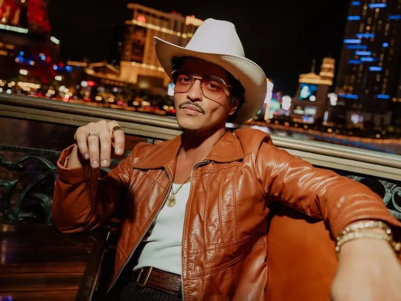 Ο Bruno Mars με καουμπόικο καπέλο και δερμάτινο τζάκετ σε νυχτερινό φόντο.