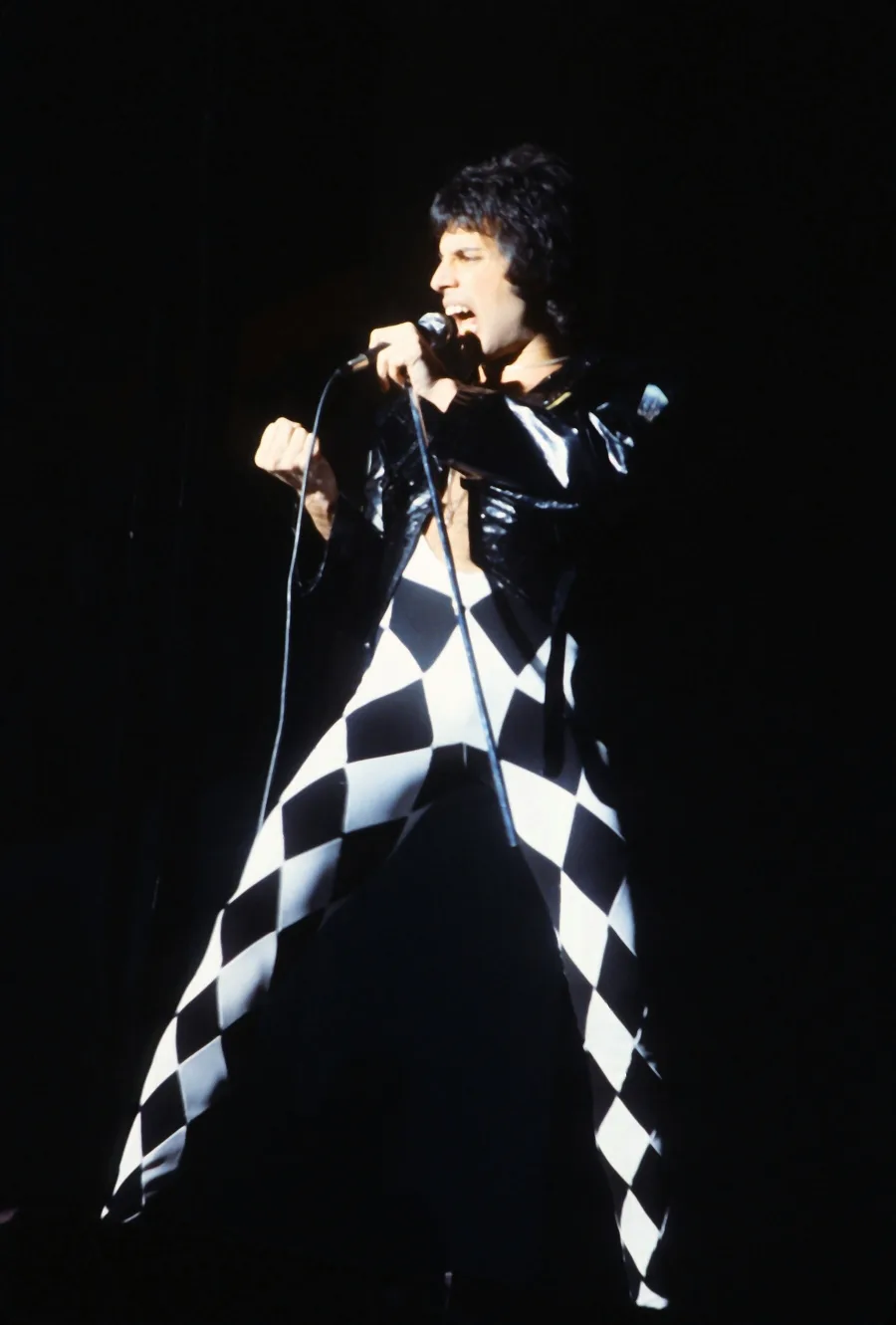Ο Freddie Mercury στη σκηνή με ασπρόμαυρο κολάν αρλεκίνου και μαύρο δερμάτινο τζάκετ.
