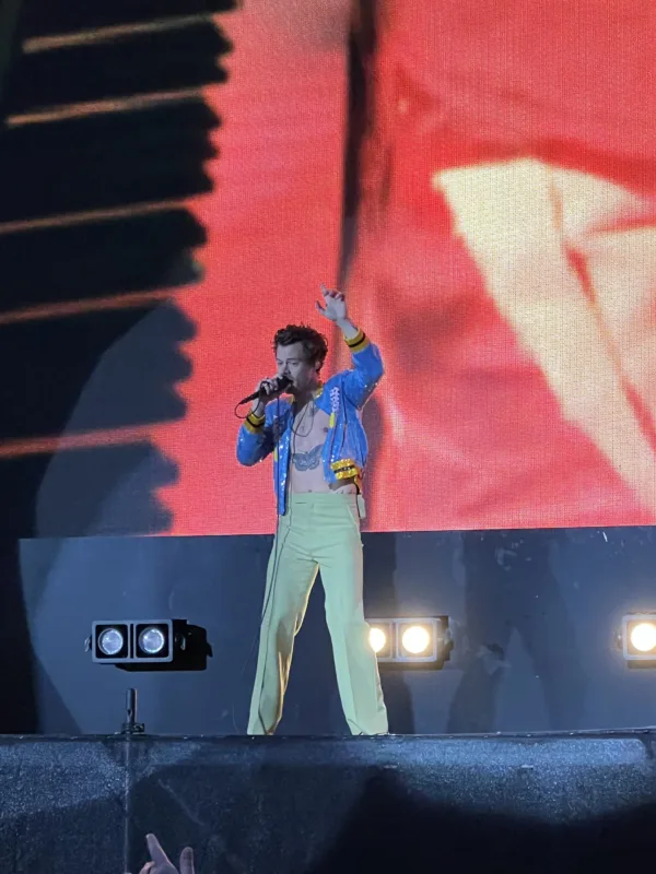 Ο Harry Styles στη σκηνή με γαλάζιο τζάκετ και κίτρινο παντελόνι.