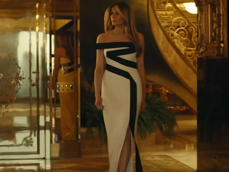 Η Melania Trump με λευκό φόρεμα και μαύρες λεπτομέρειες σε πολυτελή χώρο.