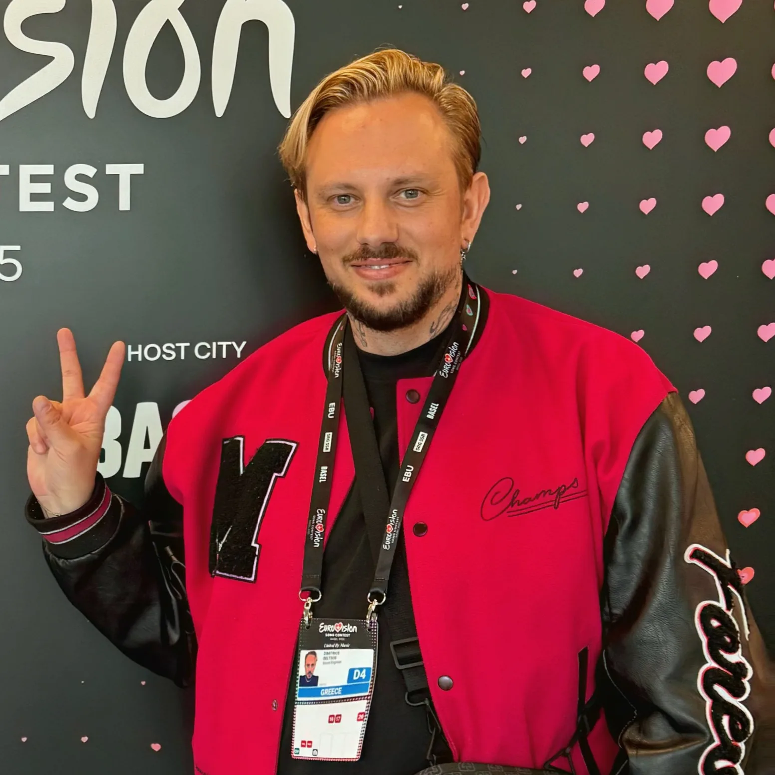 Άνδρας με κόκκινο varsity jacket και διαπιστευτήρια της Eurovision.