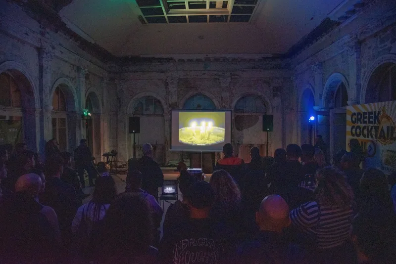Listening party σε ατμοσφαιρικό χώρο με προβολή σε οθόνη και πλήθος κόσμου.
