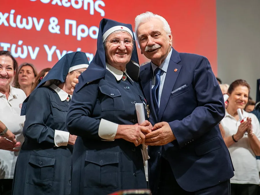 Εθελόντρια του Ελληνικού Ερυθρού Σταυρού με επίσημη στολή και άνδρας με κοστούμι σε τελετή απονομής.