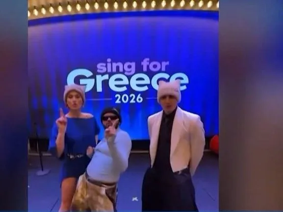 Η Evangelia, ο Ακύλας και ο Good Job Nicky ποζάρουν μπροστά από το λογότυπο Sing for Greece 2026.