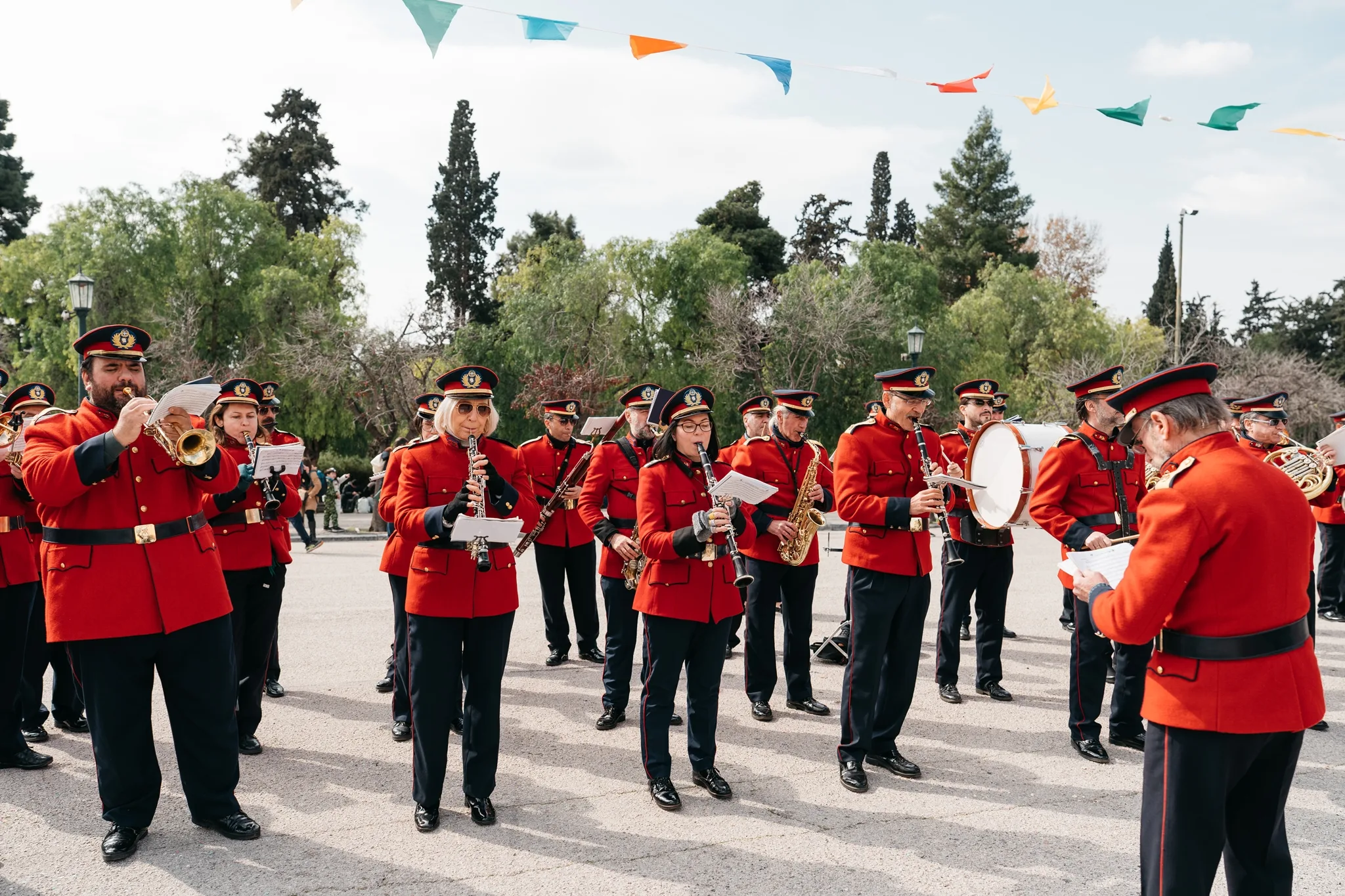 Φιλαρμονική Ορχήστρα του Δήμου Αθηναίων με κόκκινες στολές σε εξωτερικό χώρο.