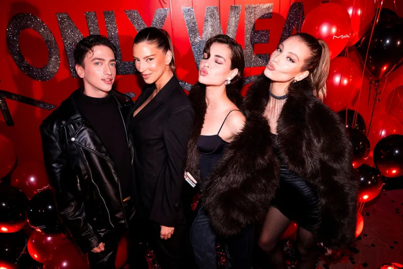 Τέσσερα άτομα ποζάρουν σε event της MAC Cosmetics με κόκκινο φόντο και μπαλόνια.