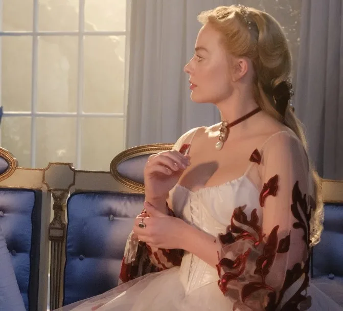 Η Margot Robbie ως Cathy με ρομαντικό χτένισμα και λευκό φόρεμα.