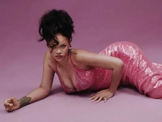 Η Rihanna ποζάρει με ροζ αστραφτερό φόρεμα σε μωβ φόντο.