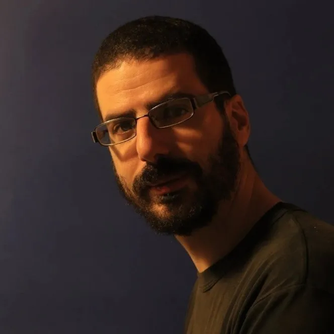 Κοντινό πορτρέτο άνδρα με γυαλιά και μούσια σε μπλε φόντο.