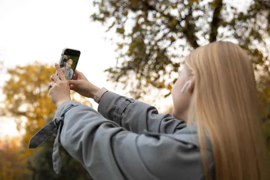 Νεαρή γυναίκα βγάζει selfie με το κινητό της σε εξωτερικό χώρο το φθινόπωρο.