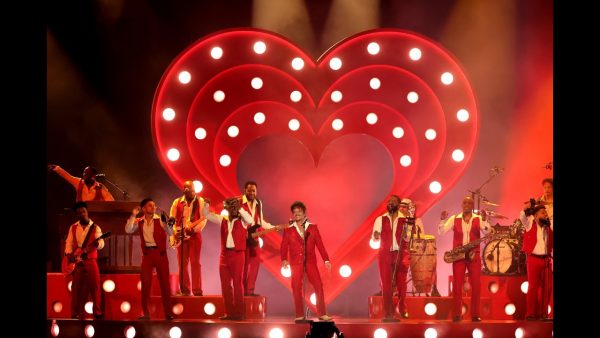 Ο Bruno Mars στη σκηνή των Grammy με το συγκρότημά του μπροστά από μια μεγάλη φωτιζόμενη καρδιά.