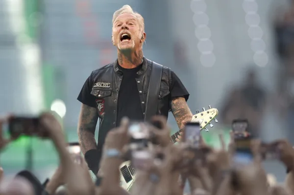 Ο James Hetfield τραγουδάει με πάθος στην σκηνή, κρατώντας την κιθάρα του μπροστά σε κοινό.