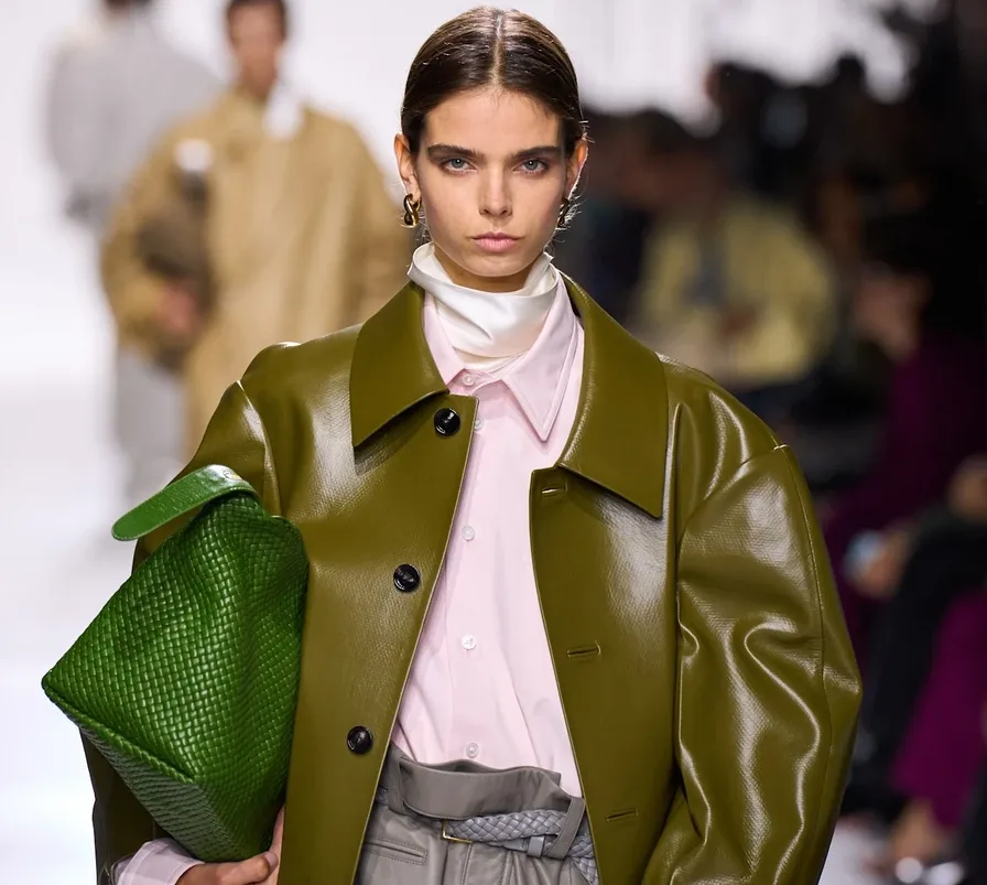 Μοντέλο σε πασαρέλα με πράσινο δερμάτινο jacket, ροζ πουκάμισο και πράσινη τσάντα.