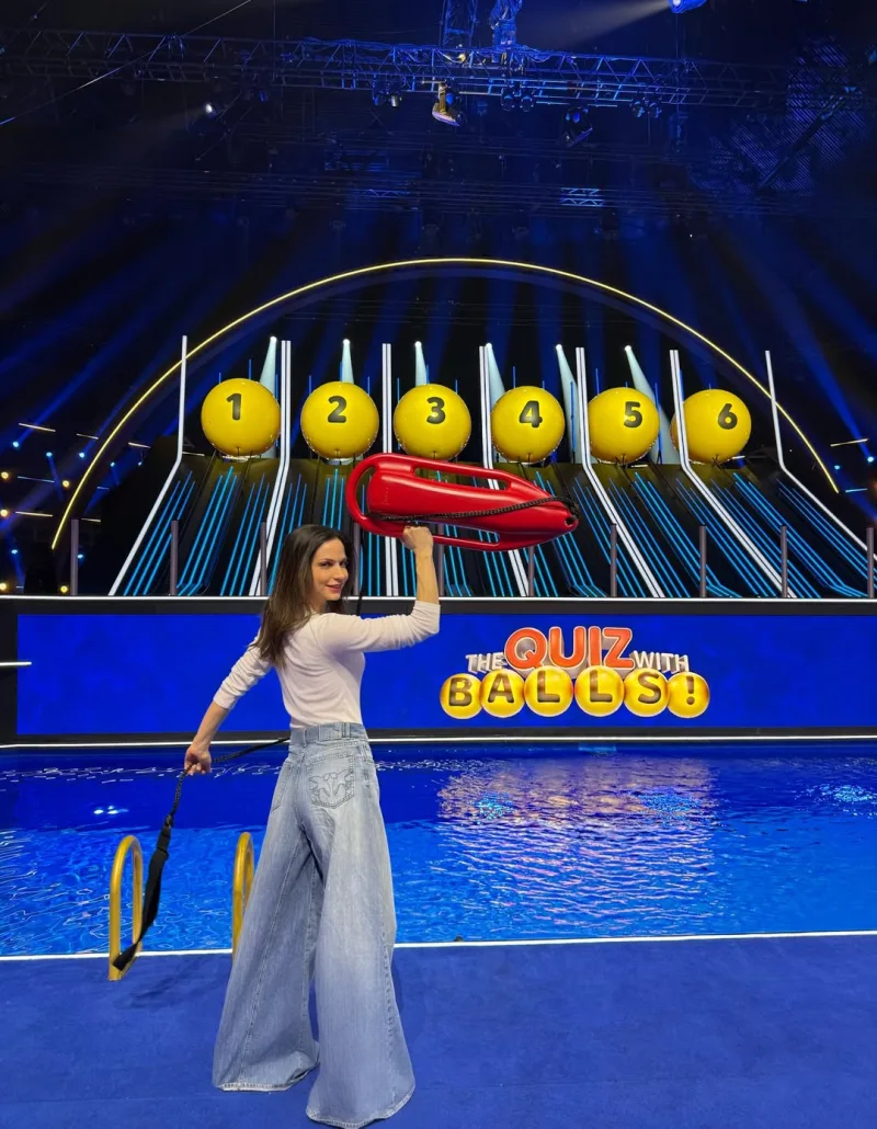 Η Κατερίνα Γερονικολού στο πλατό του «The Quiz with Balls» κρατώντας σωσίβιο και με φόντο τους αριθμημένους κρίκους.