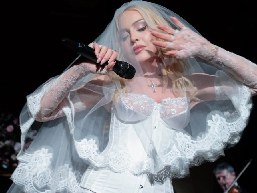 Η Madonna με νυφικό πέπλο και κορσέ τραγουδάει με μικρόφωνο, φορώντας κολιέ Swarovski.