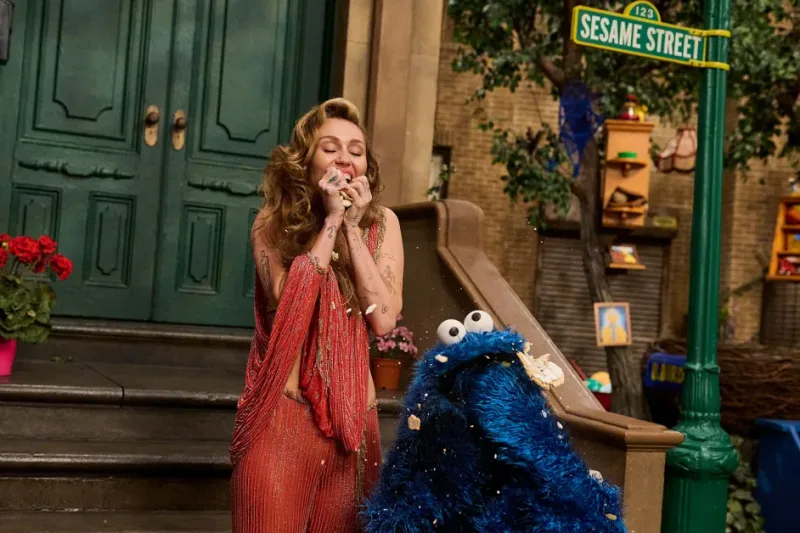 Η Miley Cyrus και ο Cookie Monster από το Sesame Street κρατούν λουλούδια.