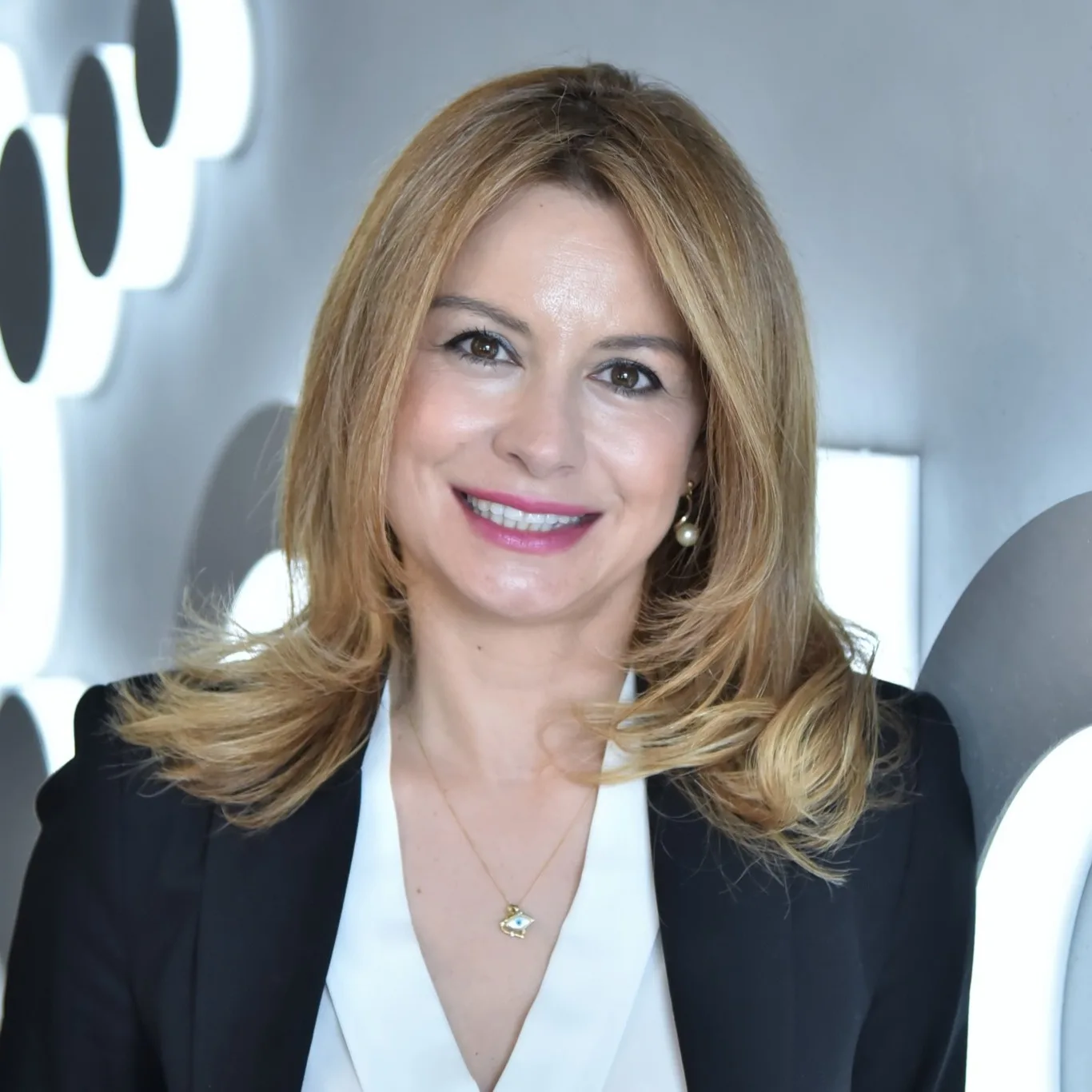 Πορτρέτο γυναίκας με ξανθά μαλλιά, μαύρο σακάκι και λευκό πουκάμισο.