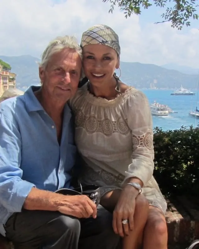 Catherine Zeta-Jones και Michael Douglas ποζάρουν χαμογελαστοί με φόντο την πολυτελή έπαυλη τους στον ποταμό Hudson.