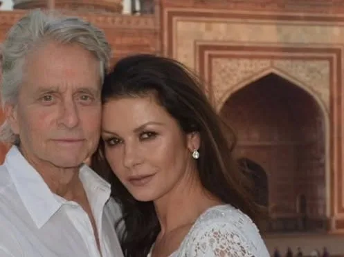 Catherine Zeta-Jones και Michael Douglas ποζάρουν χαμογελαστοί, με φόντο την εντυπωσιακή έπαυλη στον ποταμό Hudson.