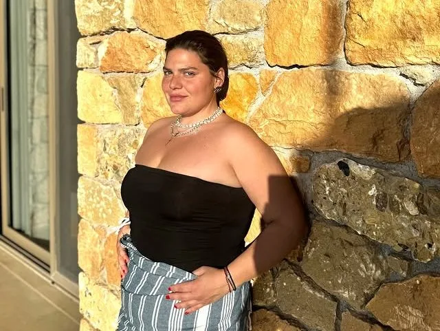 Η Δανάη Μπάρκα ποζάρει με κομψό outfit μπροστά σε πέτρινο τοίχο, προετοιμάζοντας την εμφάνισή της για τον γάμο της στη Μεσσηνία.
