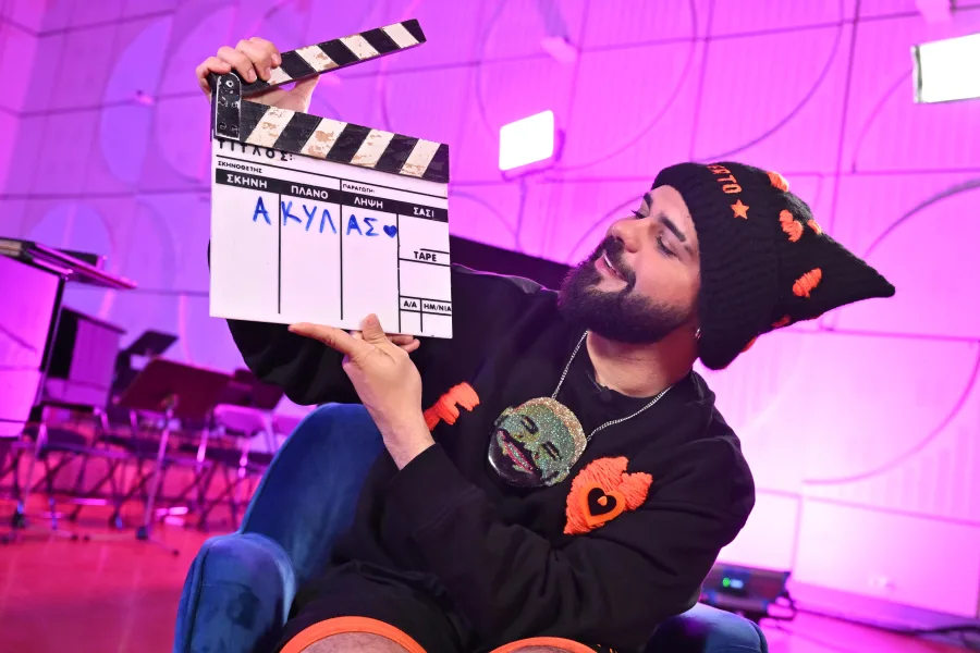 Ο Akylas κρατάει clapperboard με το όνομά του γραμμένο, κατά τη διάρκεια του Eurovision Press Day, δίνοντας μήνυμα για όνειρα.