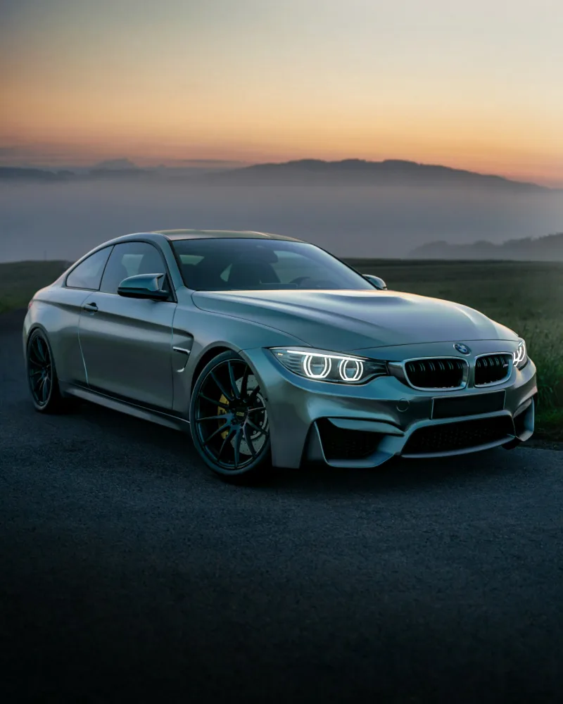 Ασημί BMW M4 coupe με αθλητικές ζάντες και φώτα ημέρας, σε φόντο ηλιοβασιλέματος, ιδανικό για αγορά αυτοκινήτου.