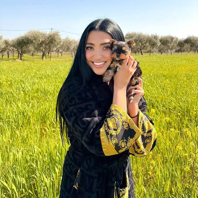 Η Anastasia ποζάρει χαμογελαστή κρατώντας ένα κουτάβι σε ένα καταπράσινο λιβάδι, προετοιμάζοντας την επιστροφή της στην Αυστραλία.
