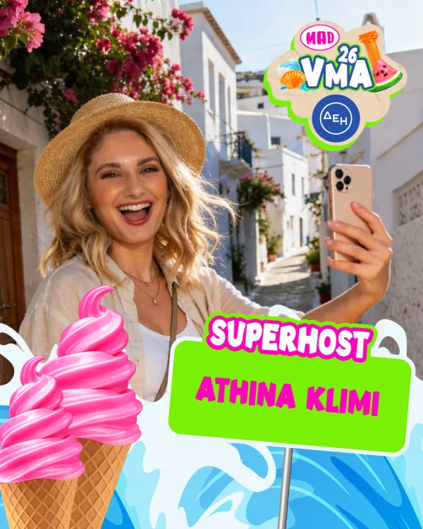 Η Αθηνά Κλίμη, Superhost των Mad VMA 2026, ποζάρει χαμογελαστή με το κινητό της σε ένα γραφικό κυκλαδίτικο σοκάκι.