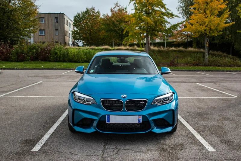 Μπλε σπορ αυτοκίνητο BMW σταθμευμένο σε πάρκινγκ, με φθινοπωρινά δέντρα και κτίριο στο φόντο.
