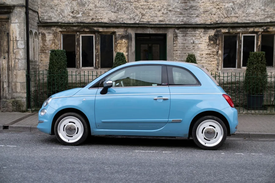 Μπλε αυτοκίνητο Fiat 500 σταθμευμένο σε δρόμο μπροστά από πέτρινο κτίριο, σχετικό με την αγορά αυτοκινήτου.