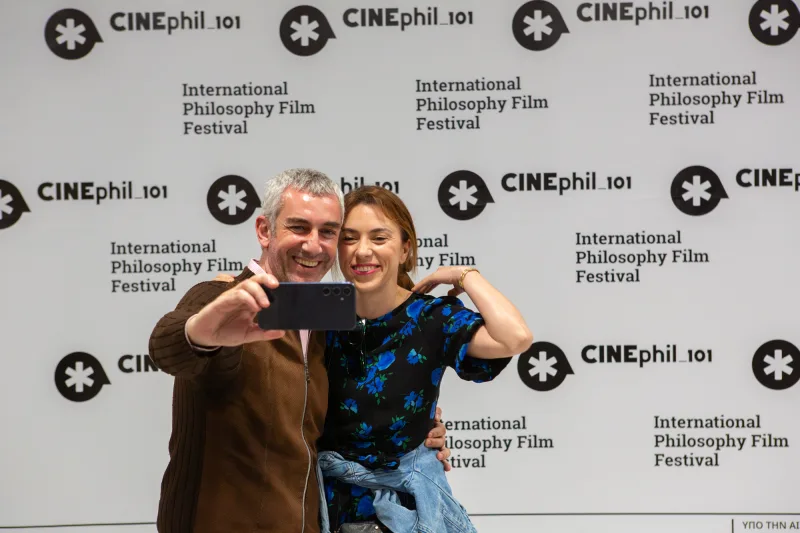 Ο άνδρας και η γυναίκα ποζάρουν για selfie μπροστά από το backdrop του 2ου CINEphil_101, του Διεθνούς Φεστιβάλ Φιλοσοφικού Κινηματογράφου.