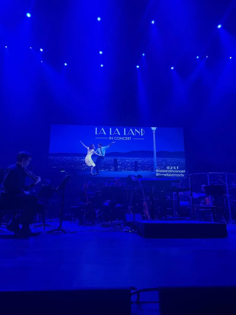 Σκηνή από τη συναυλία La La Land in Concert στη Νέα Υόρκη, με ορχήστρα και χορευτικό ζευγάρι στην οθόνη.