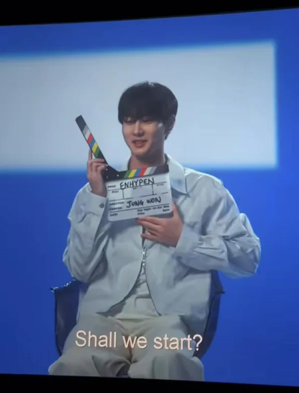 Ο Jung Won των ENHYPEN κρατάει ένα clapperboard, προετοιμάζοντας τη συναυλιακή εμπειρία για τη μεγάλη οθόνη.